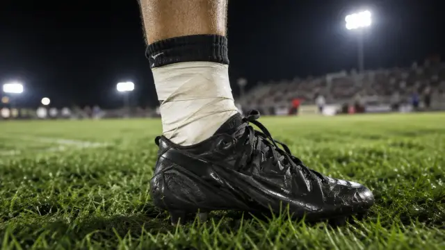 Football player's taped ankle and cleat on a grass field